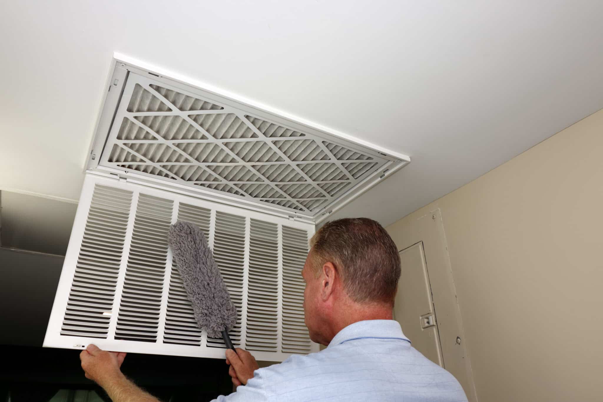 Male Dusting the Inside of a Home Furnace Intake Air Vent Grid, HVAC Inspections.